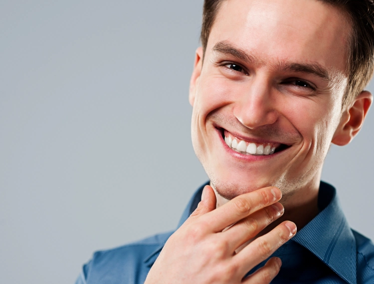 Close-up of a smiling man with hand touching his chin against a gray background.
